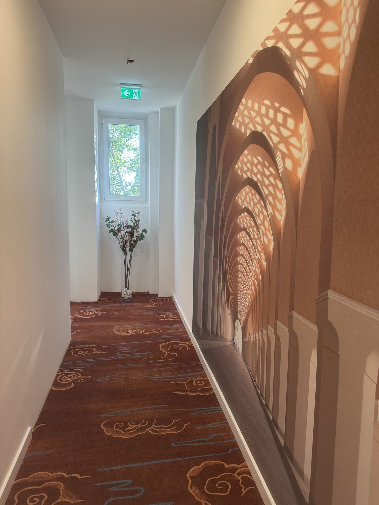 Flur mit rot gemustertem Teppich und Sonnenlicht auf der Wandgestaltung
