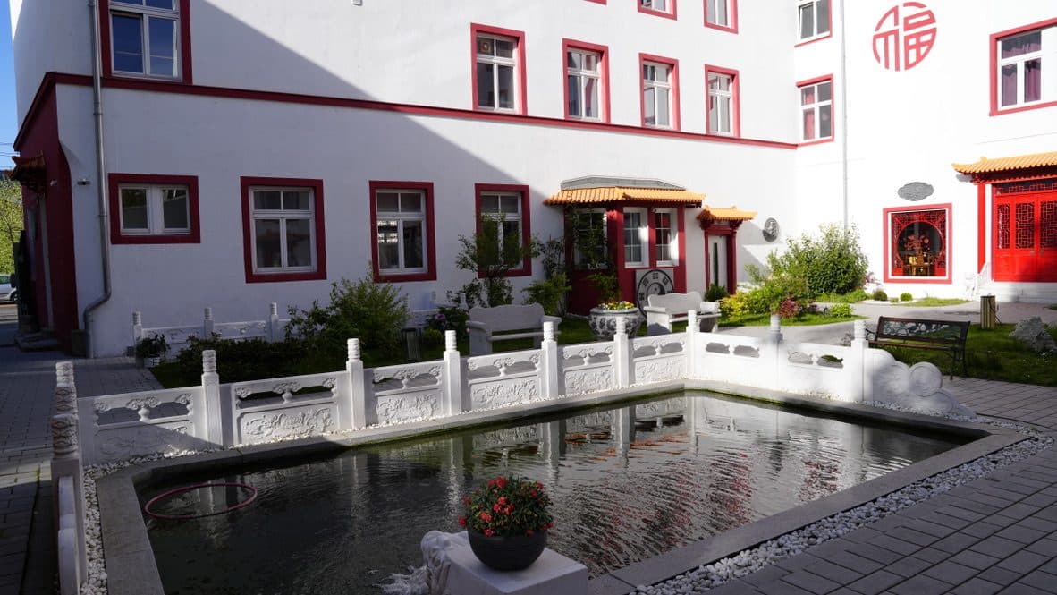 Wasserbecken mit Fontäne und weißer Steinbalustrade vor der rot-weißen Fassade