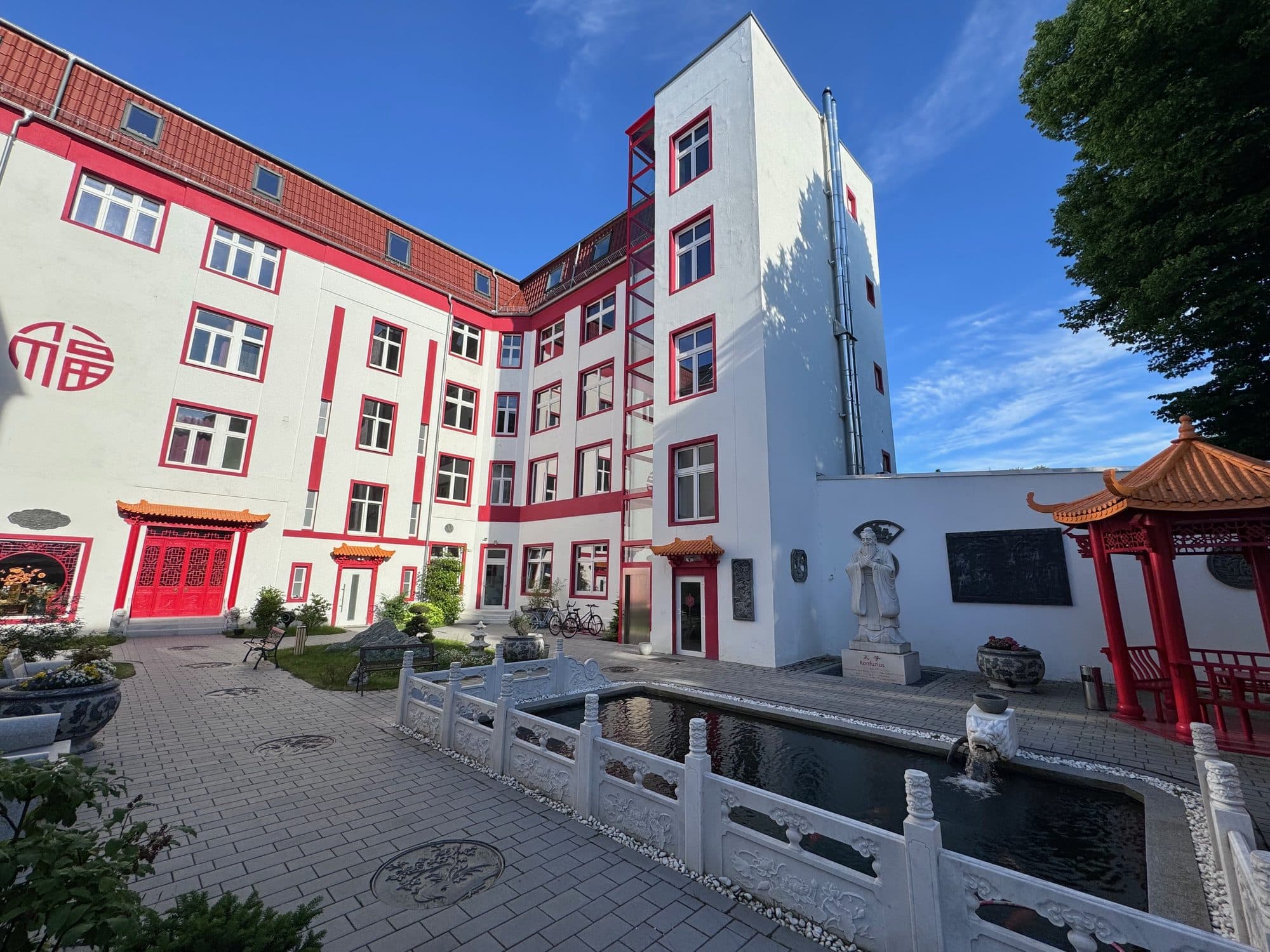 Sonniger Innenhof des ChinaCenters mit Wasserbecken, Steinbalustrade und rot-weißer Fassade